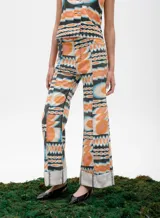 Pantalón de jean azul oscuro con corte acampanado, tiro medio y dobladillo en el ruedo. Presenta costuras marcadas en el frente y estampado abstracto en tonos grises y blancos en el interior del dobladillo.