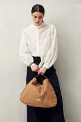 Bolso tipo hobo de poliuretano color camel, con asa corta y logo metálico plateado.