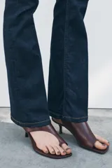 Pantalón de jean azul oscuro, de tiro medio, corte bootcut y largo hasta el tobillo. Tiene cinco bolsillos, trabillas en la cintura y cierre frontal con cremallera y botón metálico.