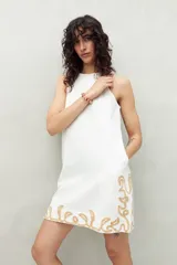 Vestido corto blanco de algodón con bordado artesanal color dorado en el ruedo. Tiene cuello alto y silueta recta.