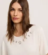 Remera blanca de viscosa con cuello redondo, mangas cortas y apliques de strass en el cuello.