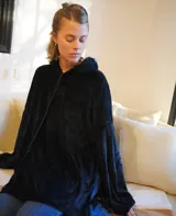 Buzo tipo canguro oversize de tela plush, color azul claro. Presenta capucha, cierre frontal parcial con cordón turquesa y bolsillos canguro frontales. Las mangas son largas y abullonadas con puños ajustados.