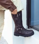 Bota de caña alta color negro, realizada en cuero encerado, con hebillas en la caña y herrajes de níquel. El fondo está realizado artesanalmente, es de suela, y es negro. El interior está forrado en forrería vacuna.