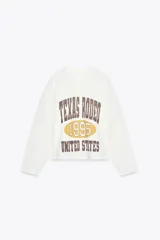 Sudadera blanca de algodón con cuello redondo y mangas largas. Estampado frontal con texto "Texas Rodeo 1995 United States" en color marrón.