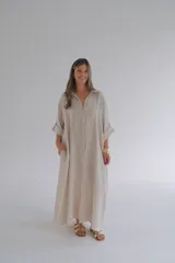Vestido camisero largo color beige, de lino, con cuello camisero, mangas largas con puños arremangados, cierre frontal con botones y bolsillos laterales.