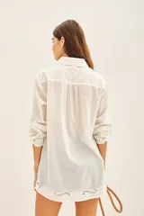 Camisa blanca de algodón con fit amplio, cuello y cartera frontal, y bordados calados en el frente, mangas y espalda. Posee tajos laterales y presillas internas para regular el largo de las mangas.