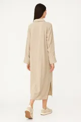 Túnica midi color beige de lino, corte holgado, manga larga, cuello camisero y cierre frontal con botones.