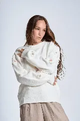 Sweater color crema de hilado frizado con cuello redondo y mangas largas. Presenta apliques de flores en los hombros y mangas.
