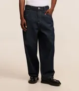 Pantalón de jeans azul oscuro, corte amplio tipo skater, con cintura con trabillas, cierre tradicional, bolsillos y costuras contrastantes.