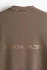 Buzo de algodón pesado color marrón con efecto lavado e interior cepillado suave. Modelo con diseño estampado, cuello redondo y hombros caídos. Remate acanalado en cuello, puños y bajo. Corte holgado.