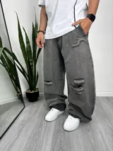 Pantalón de jean gris oscuro, corte holgado con roturas en las rodillas.