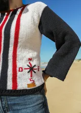Sweater tejido a mano en algodón reciclado, color blanco con detalles en azul marino y rojo. Presenta cuello redondo, mangas largas en color azul marino y un diseño de brújula bordada en el frente.