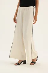 Pantalón de lino color beige, de corte ancho, con cintura elástica y ribete negro en los laterales con tajos en el ruedo.