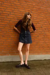 Pollera mini de denim color azul oscuro, con corte evasé y tiro alto. Presenta botonadura frontal metálica y bolsillos delanteros con solapa decorativa.