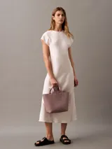 Mini cartera tote Calvin Klein color rosado, confeccionada en poliuretano con doble asa de mano y correa de hombro ajustable extraíble. Incluye cierre con botón a presión y bolsillo interior para tarjeta.