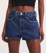 Short de jean azul oscuro, de tiro alto, con bolsillos delanteros y traseros, cierre con botón y cremallera, trabillas dobles y terminación deshilachada.