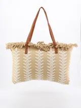 Bolso tipo tote color beige con diseño geométrico en blanco y flecos en la parte superior. Tiene doble asa de hombro marrón.