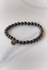 Pulsera elástica de piedras naturales color marrón con dije circular dorado con la palabra "AIRE" grabada.