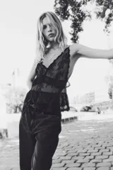 Top negro de breteles finos, confeccionado en encaje floral transparente. Presenta escote en V con botones forrados al frente, un ribete de volados bajo el busto y un segundo volado doble en el bajo.