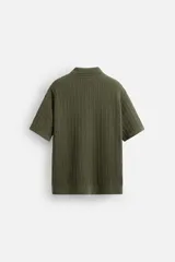 Camisa verde militar de punto con estructura abierta, corte regular fit, cuello solapa, manga corta y cierre frontal con botones.