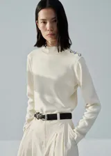 Sweater color crema de punto fino con cuello perkins y manga larga. Presenta detalle de botones metálicos en el hombro.