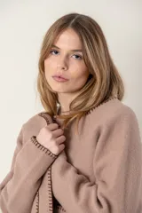 Chaqueta corta color gris oscuro confeccionada en lana merino hervida, con cuello redondo, mangas largas y bolsillos frontales. Presenta detalle de flecos en el ruedo.