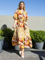 Vestido maxi con estampado floral en tonos amarillos, con mangas amplias y cinturón a juego.