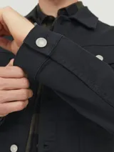 Chaqueta de denim negra de manga larga con puños abotonados. Cierre con botones frontales y bolsillos en el pecho.
