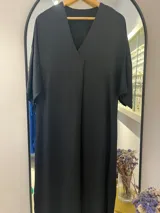 Túnica o vestido negro de manga corta y corte holgado, con escote en V profundo y cruce frontal en la parte superior.