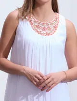 Vestido blanco de gasa con escote redondo bordado con apliques metálicos. Tiene forro interno a tono y ruedo en capas asimétricas.