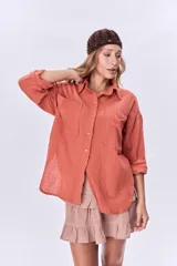 Camisa color coral de corte holgado, con cuello clásico, cierre frontal con botones, mangas largas con puños abotonados, dos bolsillos de parche en el pecho y ruedo asimétrico.