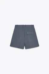 Bermudas de tiro alto color gris, con bolsillos delanteros y falso bolsillo con solapa en la espalda. Detalle de pinzas en el delantero y cierre frontal con cremallera y gancho metálico.