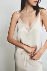 Conjunto de pijama color crema con detalles de encaje en el top. El top es de tirantes finos y el pantalón es largo con volados en el ruedo.