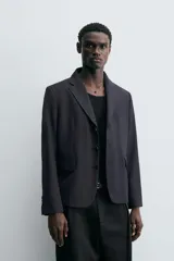 Blazer negro de corte relaxed fit confeccionada en tejido con lana. Cuello con solapas de muesca y manga larga acabada en puño con botones. Bolsillos de vivo en pecho y de solapa en cadera. Detalle de bolsillo interior. Bajo con aberturas en espalda. Cierre frontal de botonadura.