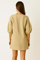 Vestido corto color beige, con escote en V y mangas globo de tres cuartos con elástico en los puños.