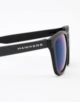 Gafas de sol unisex Hawkers, con montura cuadrada negra con textura y lentes espejados azules.