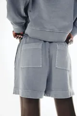 Short gris de felpa de algodón con efecto lavado, corte holgado, cintura elástica con cordón ajustable, bolsillos laterales y traseros, y aberturas laterales en el ruedo.
