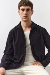 Camisa de manga larga color negro con finas rayas verticales, cuello inglés, tapeta clásica, bolsillo superior abierto, canesú con pliegue de caja en la espalda y bajo redondeado.