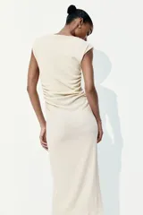 Vestido midi color crema, de punto arrugado, con mangas japonesas, escote barco y laterales fruncidos que crean un efecto drapeado.