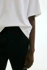 Pantalón negro tobillero con pliegues, corte ajustado, cierre con botón, bolsillos laterales y bolsillos atrás ribeteados con botón.