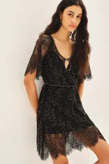 Vestido corto negro con escote en U y mangas cortas, confeccionado en encaje bordado a mano con mostacillas y lentejuelas. Tiene escote gota en el delantero y en la espalda, cinturón bordado y viso al tono con breteles regulables y puntilla en el escote.