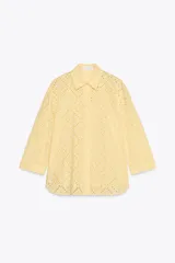 Camisa amarilla de cuello solapa y manga larga acabada en puño. Detalle de bordados perforados a tono. Cierre frontal con botones ocultos por solapa.