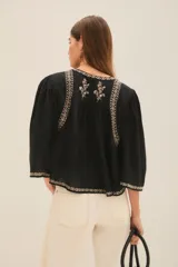 Camisa blanca de algodón con bordado negro en el ruedo, corte amplio y largo corto. Escote redondo y mangas largas abullonadas.