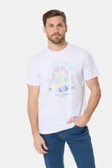 Remera blanca de manga corta con cuello redondo y un estampado gráfico frontal que simula un paisaje costero con un sol naciente o poniente, rodeado por texto circular que dice "SURF - LIFE UNDER THE SUN - CLUB".