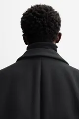 Abrigo negro regular fit confeccionado en paño con lana. Tiene cuello con solapas de muesca, manga larga, bolsillos de solapa en la cadera, bolsillo interior, abertura en el centro de la espalda y cierre frontal con botonadura.