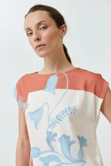 Blusa sin mangas con estampado floral en tonos celeste y naranja sobre fondo blanco. Presenta cuello redondo y corte recto.