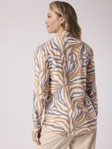 Camisa de manga larga con estampado de cebra en tonos beige, marrón y lila. Tiene cuello clásico, cierre con botones y un bolsillo en el pecho.