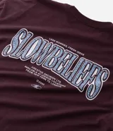 Remera de manga corta color bordó, con cuello redondo y corte relaxed. Presenta un estampado de lettering en la parte delantera con la palabra "SLOWBELIEFS" en blanco y azul, y un estampado más grande en la espalda. Confeccionada en algodón certificado BCI.