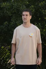 Remera color beige de manga corta con cuello redondo y estampado de un sol con montañas en el pecho.
