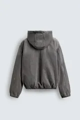 Cazadora gris de algodón con efecto lavado, corte relaxed fit, cuello con capucha ajustable, manga larga, bolsillos frontales tipo canguro, acabados con elástico y cierre frontal de cremallera.